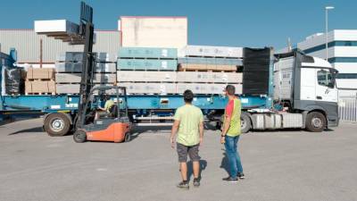 Dos operarios logísticos de la central de compras y servicios ajustan la carga de la plataforma para optimizar al máximo el espacio y la carga.